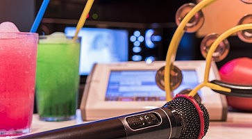 Black microphone in karaoke club, with remote controller, melon and strawberry soda drinks, yellow tambourine and screen for singing music on stage party.
